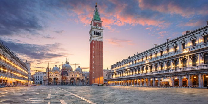 Der Markusplatz in Venedig bei Sonnenuntergang mit dem Glockenturm und historischen Gebäuden vor der Kulisse eines farbenfrohen Himmels.