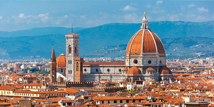 Blick auf Florenz, Italien, mit der Kathedrale von Florenz mit ihrer ikonischen roten Kuppel, umgeben von einer Stadtlandschaft unter einem klaren blauen Himmel.