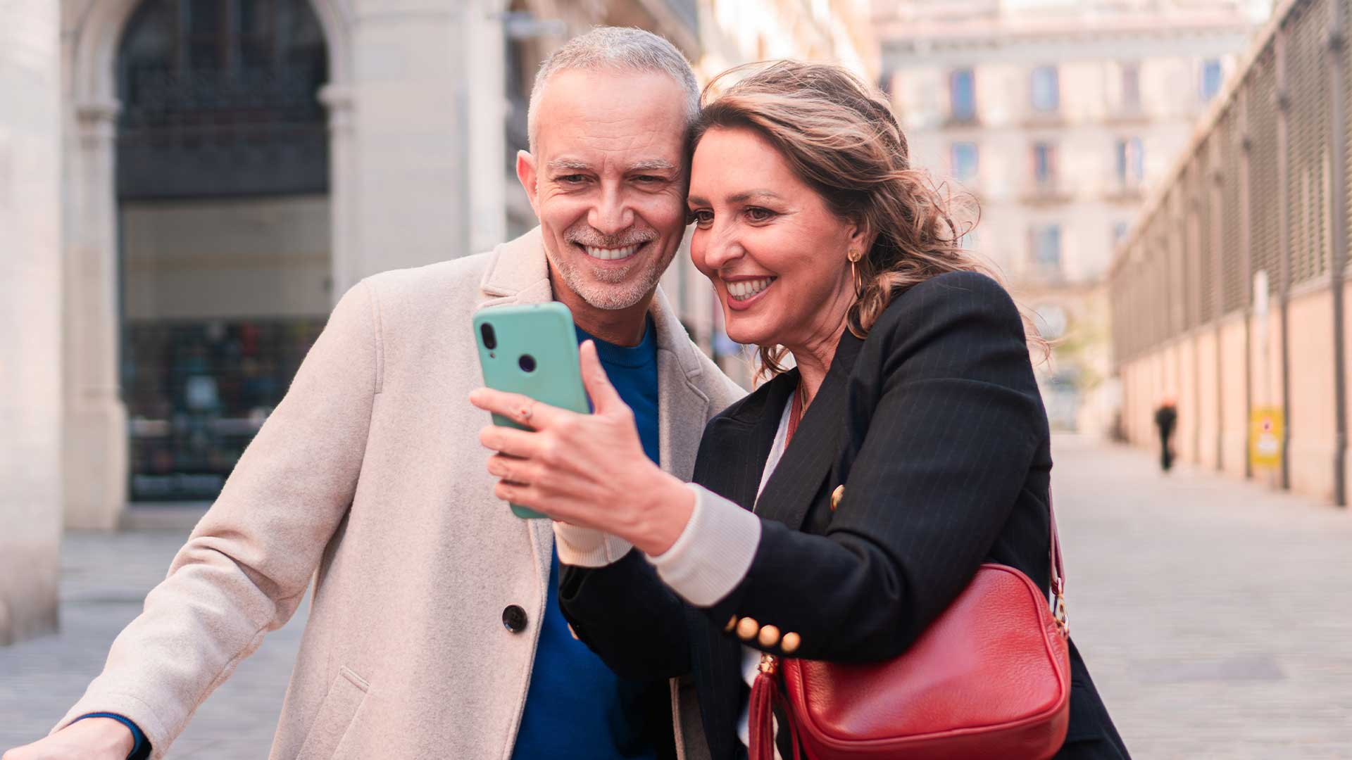 Ein Mann und eine Frau lächeln, während sie auf einer Stadtstraße gemeinsam ein Selfie machen.