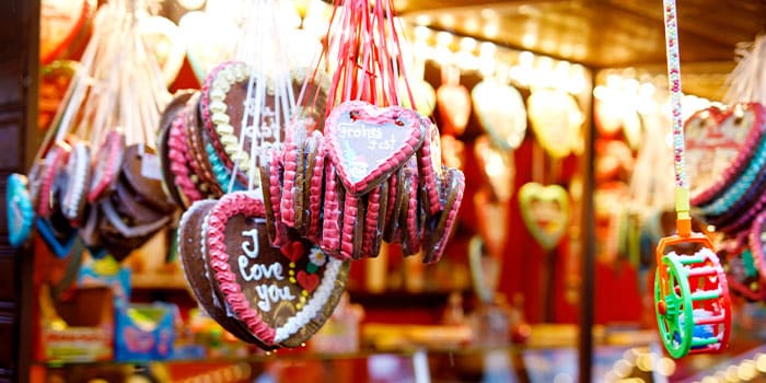 An einem festlichen Marktstand hängen bunte Lebkuchen in Herzform. Auf einem Keks steht in Zuckerguss „Ich liebe dich“.