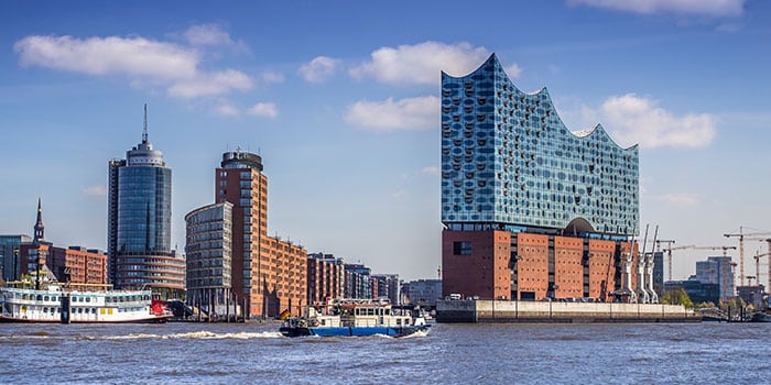 Blick auf die Elbphilharmonie mit Booten auf der Elbe und modernen Gebäuden unter blauem Himmel in Hamburg, Deutschland.