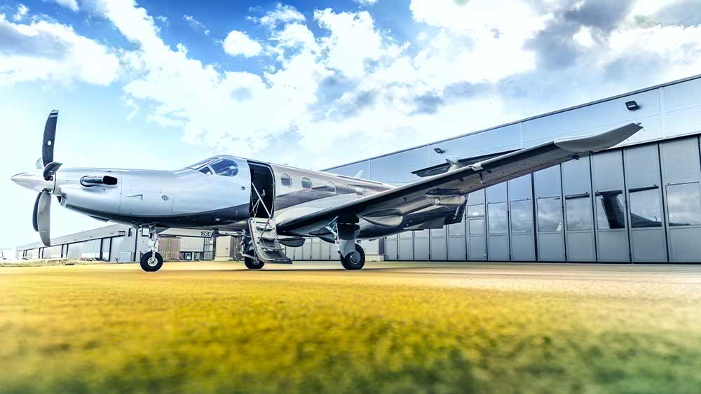 Ein kleines Privatflugzeug steht unter einem teilweise bewölkten Himmel auf dem Rollfeld in der Nähe eines Hangars.