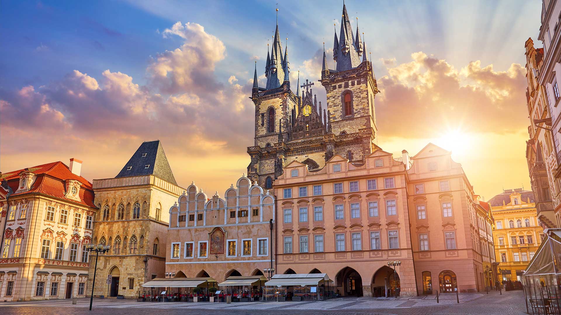 Altstädter Ring in Prag mit der Teynkirche, die unter einem teilweise bewölkten Himmel im Sonnenlicht badet.