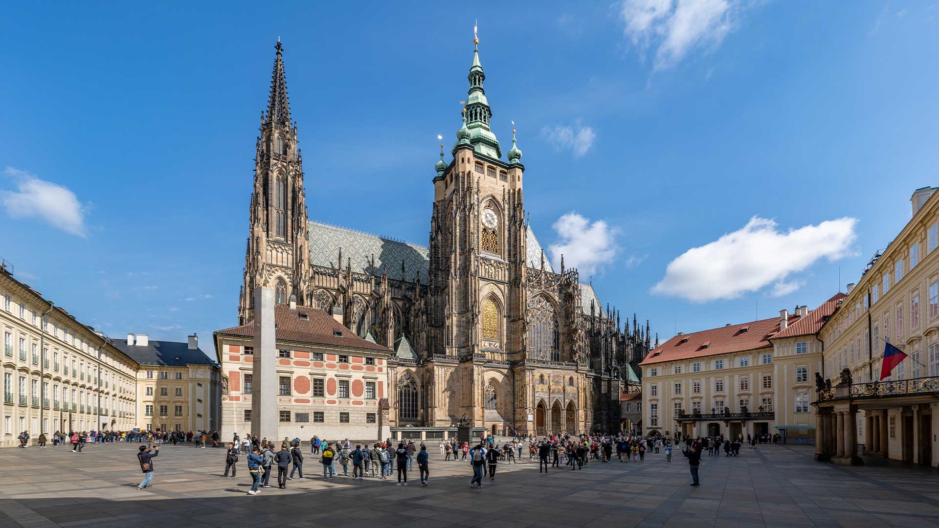 Eine große Kathedrale und historische Gebäude umgeben einen öffentlichen Platz voller Menschen unter einem klaren blauen Himmel.